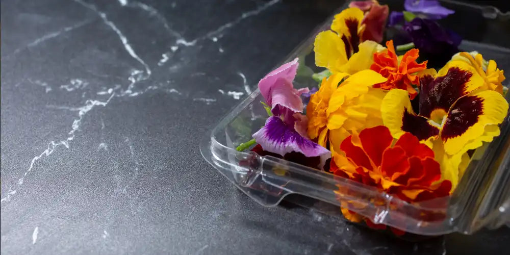 Clear plastic container with colourful edible flowers on a dark marble surface